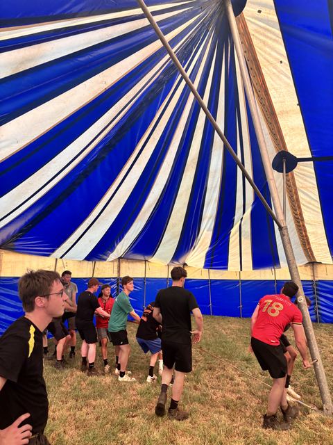 Helpers trekken samen de mast van de grote tent recht